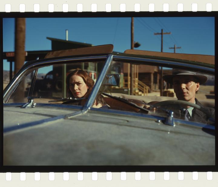 A man in a hat and a woman are sitting in a convertible car.