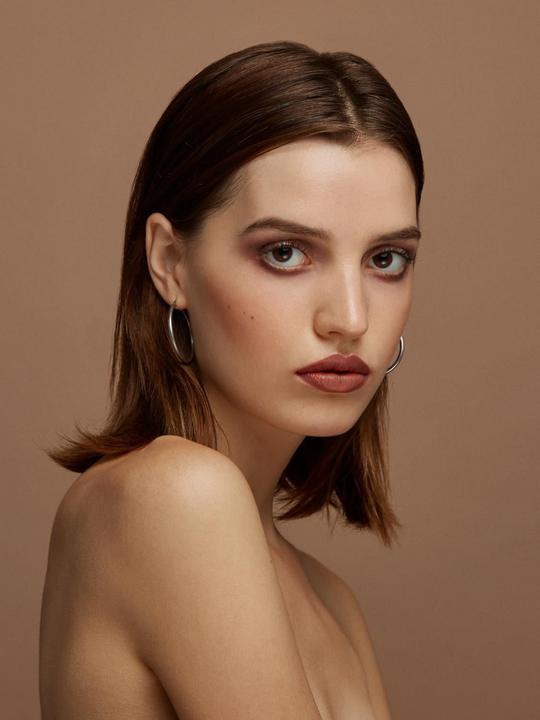 A woman with dark hair and hoop earrings looks directly at the viewer.