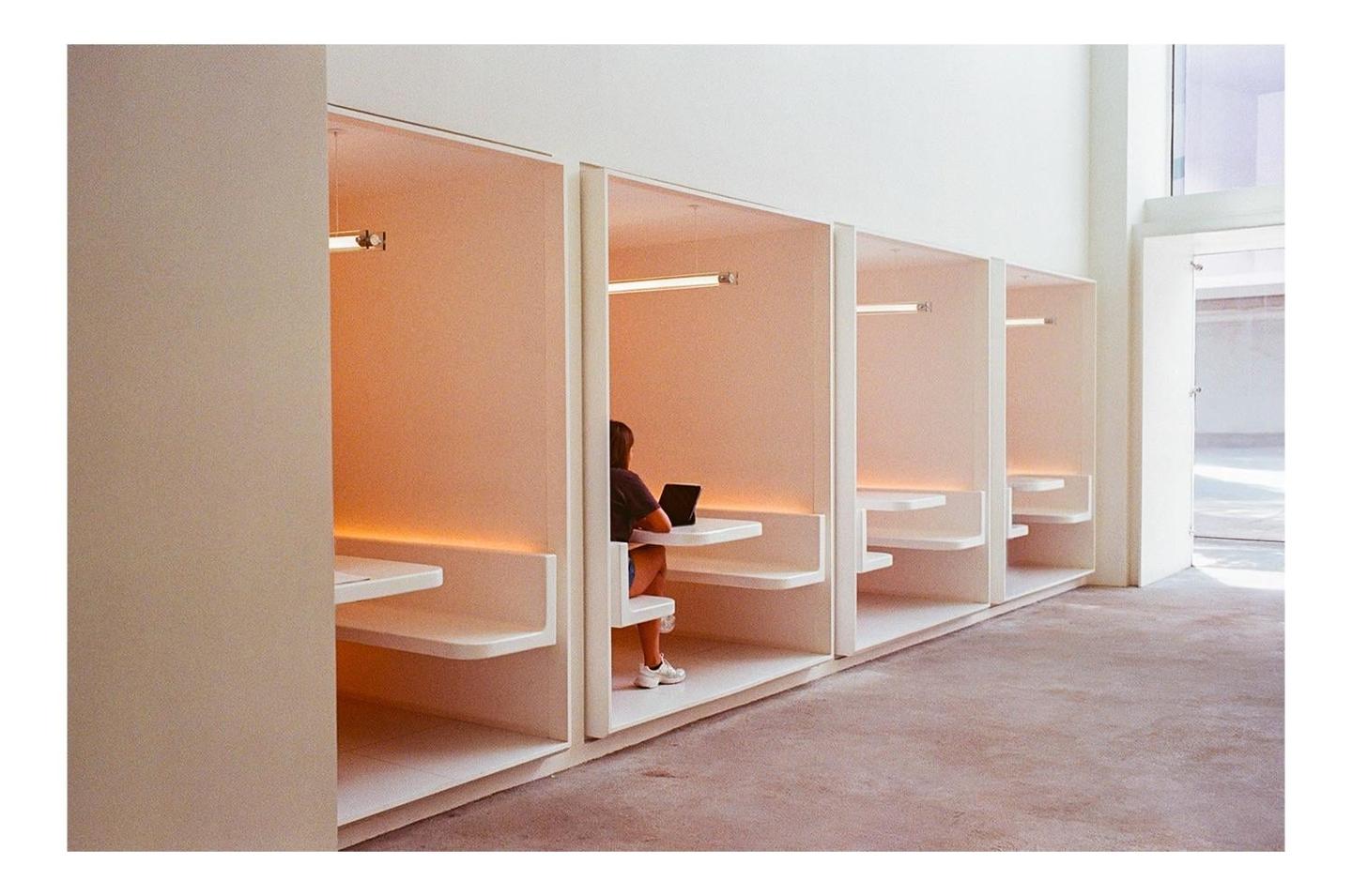 A person sits in a booth with a laptop, illuminated by warm light.