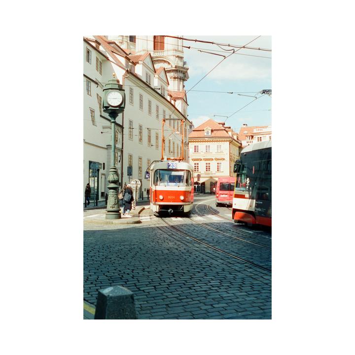 A red and white tram travels on a cobblestone street lined with buildings under a bright sky.