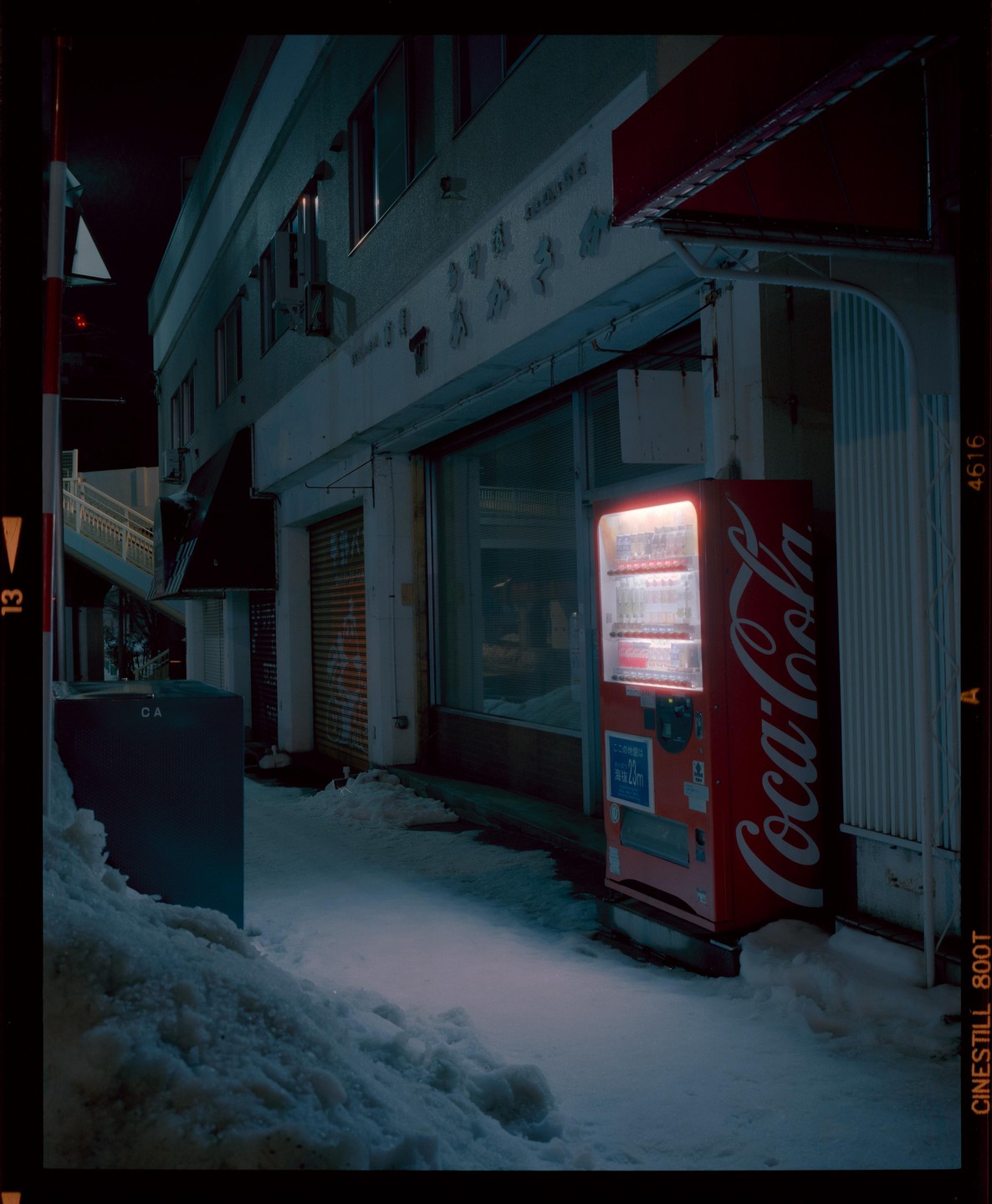 A red Coca-Cola vending machine glows on a snowy street at night.