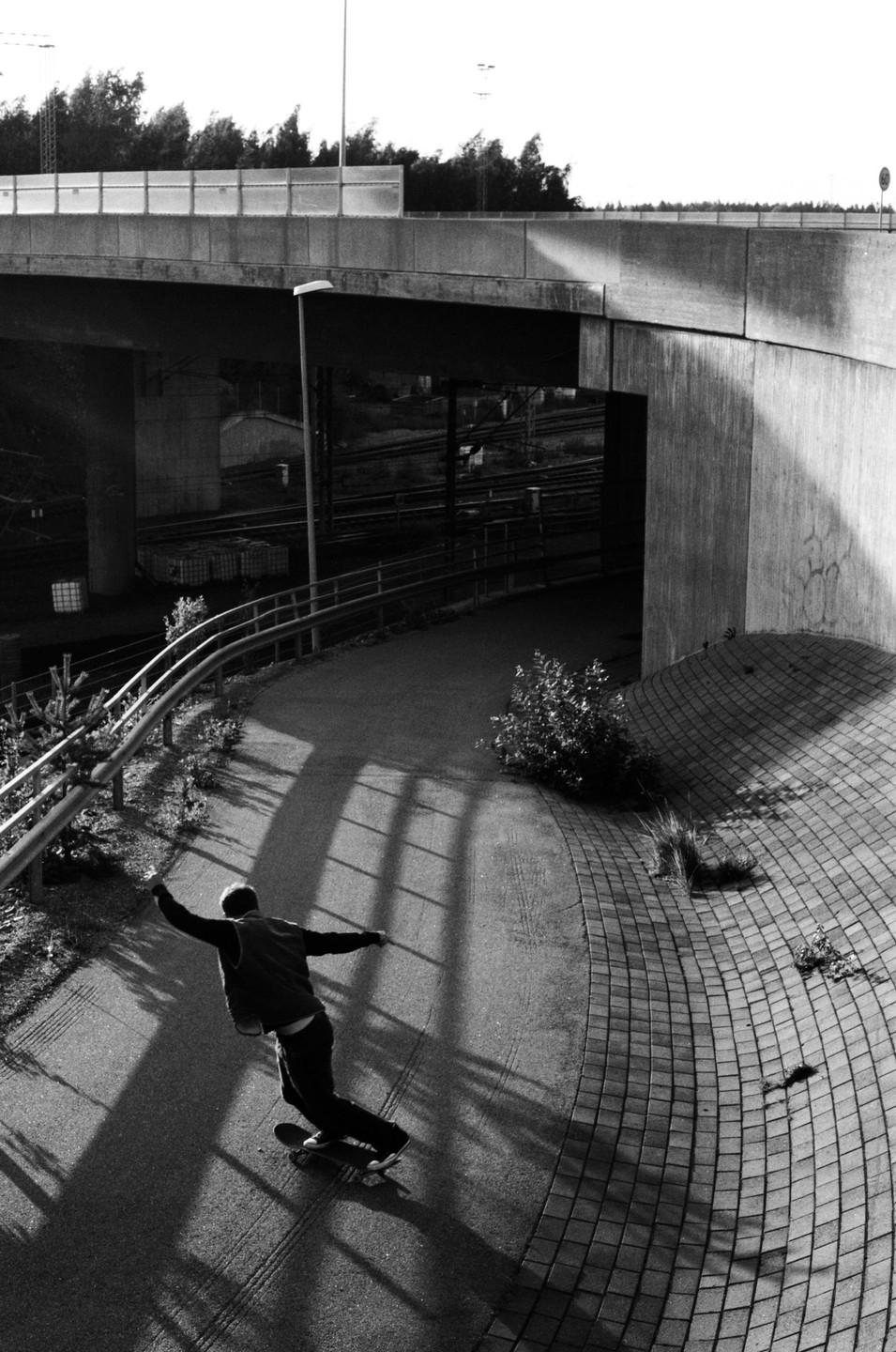A man on a skateboard performs a powerslide on a paved path under a concrete overpass.