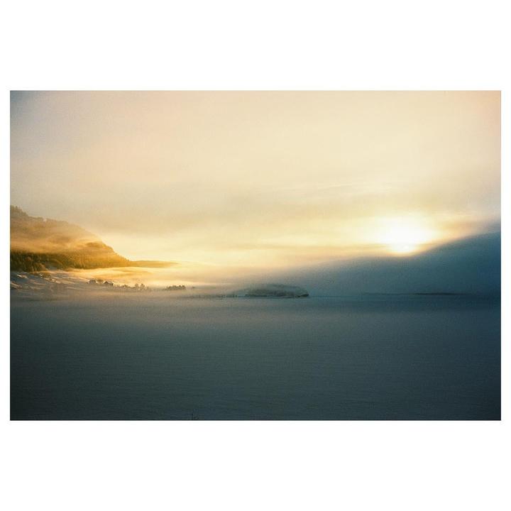 A hazy winter landscape shows a sunlit mountain and a frozen lake.