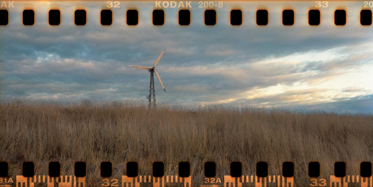 A wind turbine stands in a field of tall grass under a cloudy sky.