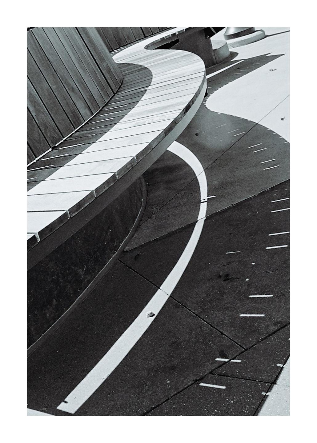 A curved wooden bench casts a shadow on the ground, which has a white line painted on it.
