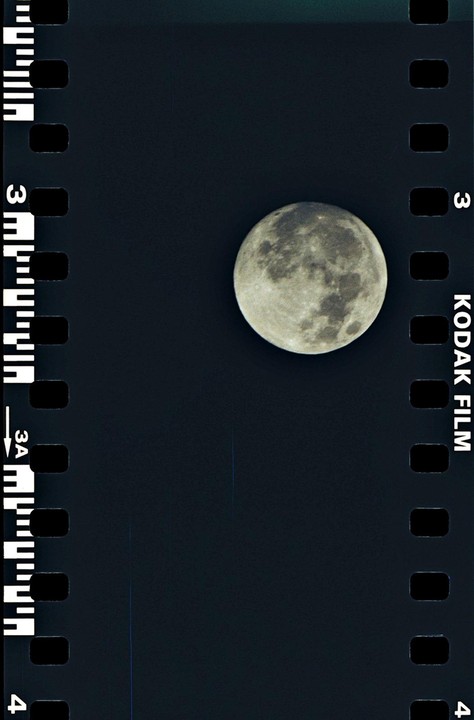 A full moon is visible against a dark sky, framed by the sprockets and text of a film strip.