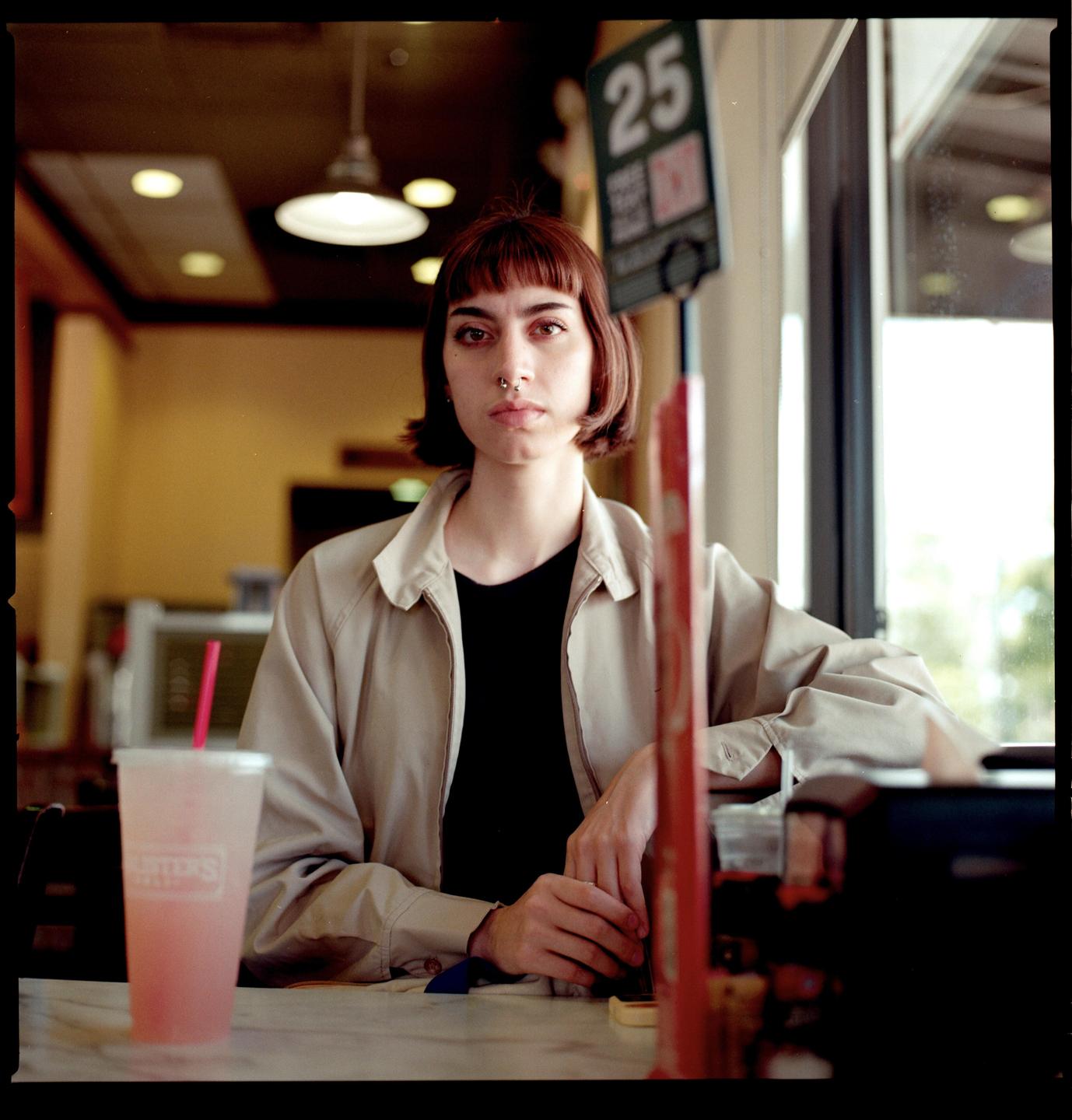 A woman with a nose ring sits at a table with a drink.