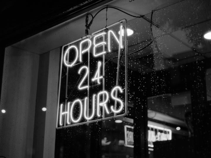 A neon sign that reads "OPEN 24 HOURS" hangs in a window covered in raindrops.