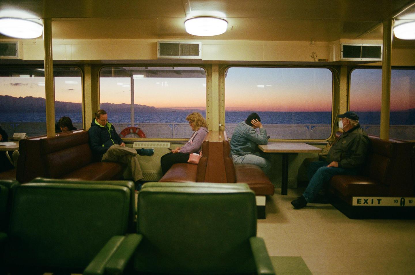 People sit inside a ferry with a sunset visible through the windows.