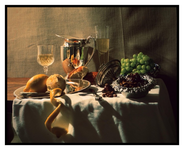 A still life arrangement features fruit, nuts, bread, and drinks on a table.