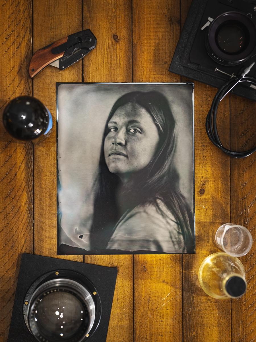 A black and white portrait of a woman is surrounded by photography equipment and a knife on a wooden surface.
