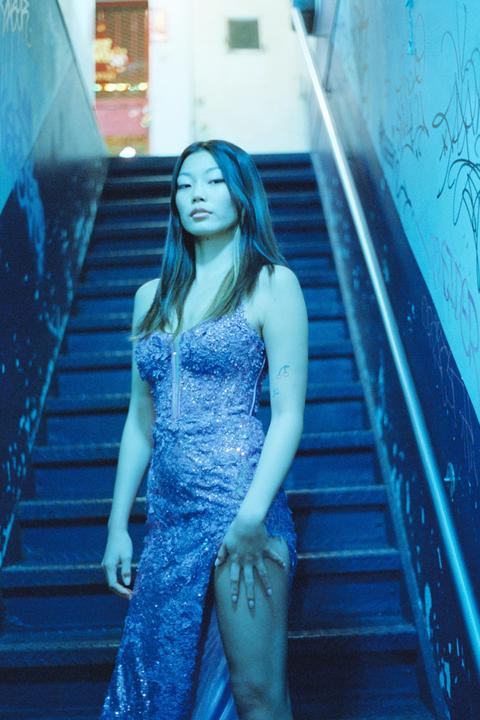 A woman in a sequined dress stands on a staircase with blue lighting.