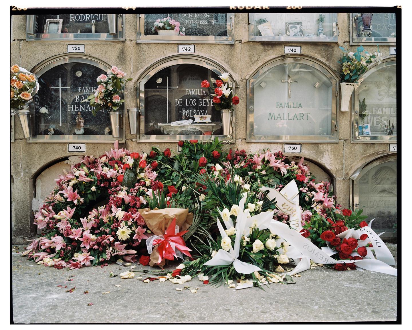 A wall of crypts with glass doors is adorned with numerous bouquets of flowers and ribbons.