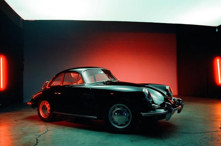 A black vintage car is parked in a studio with red and blue lighting.