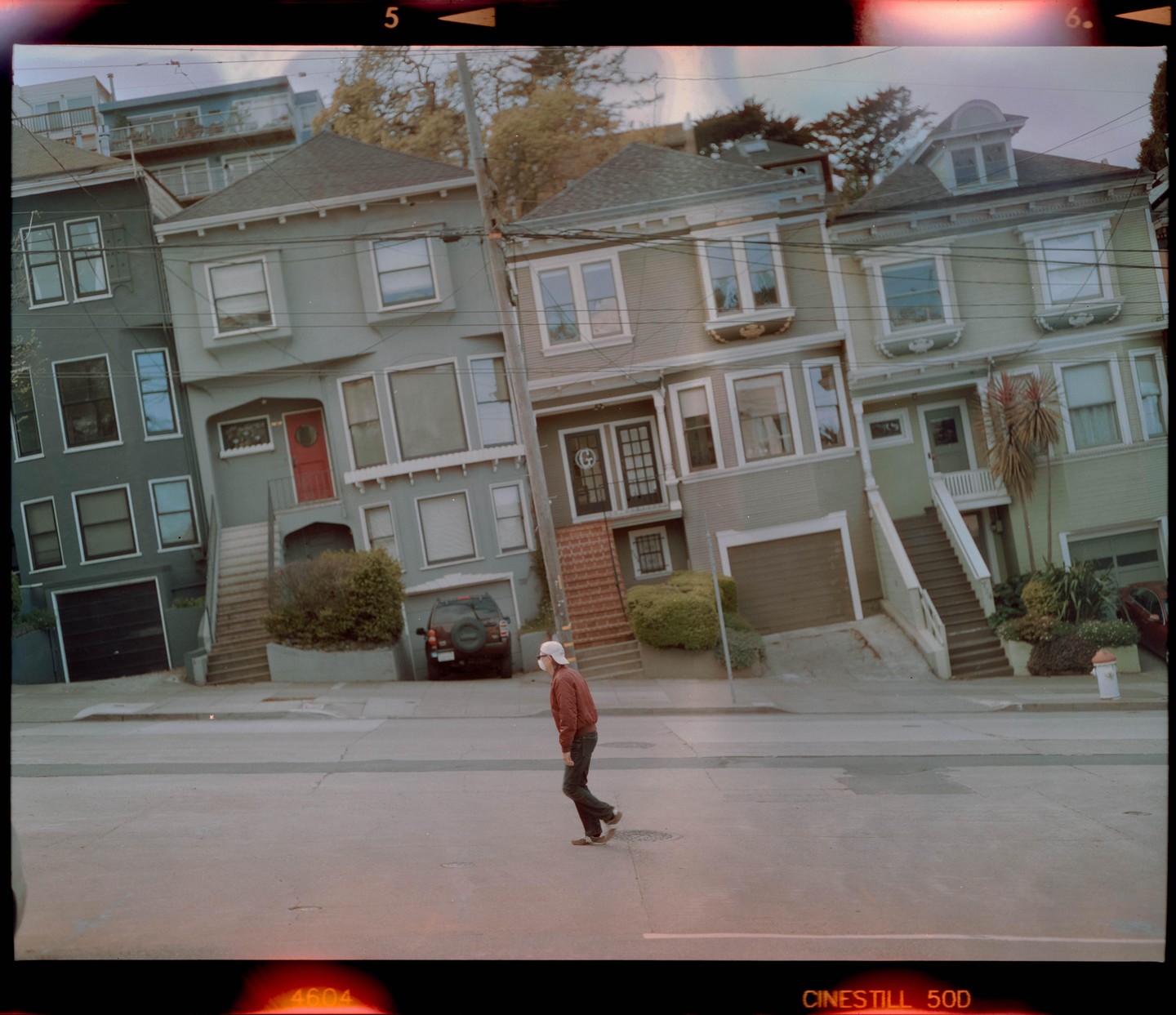 A man walks across a street in front of several houses on a steep hill in San Francisco.