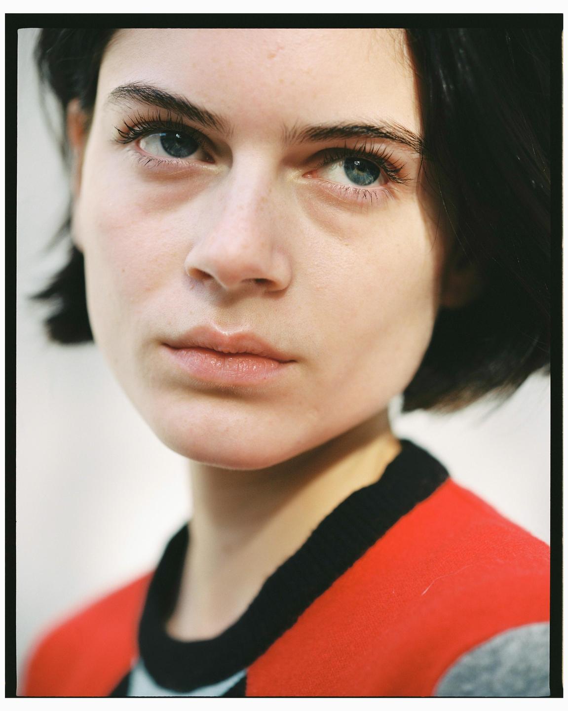 A woman with short dark hair and blue eyes looks directly forward.