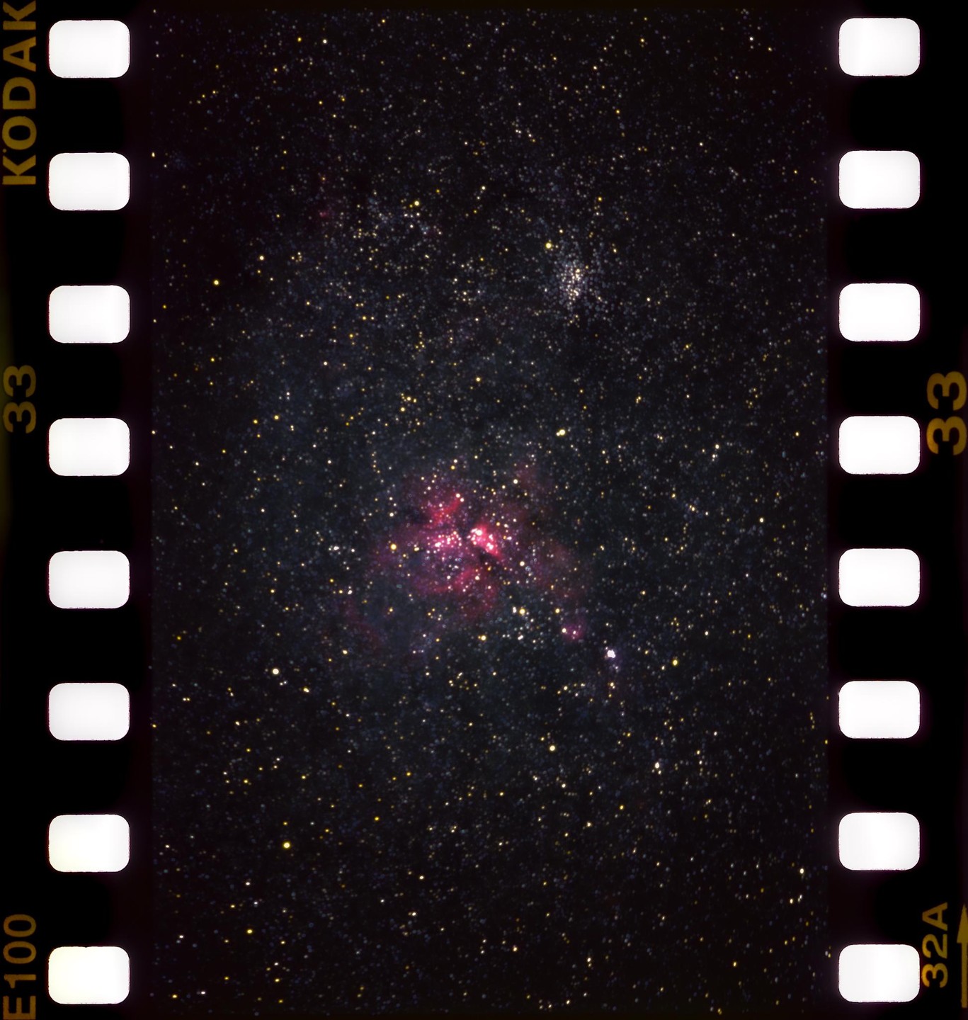 A nebula with pink and red hues is visible among many stars in the night sky.