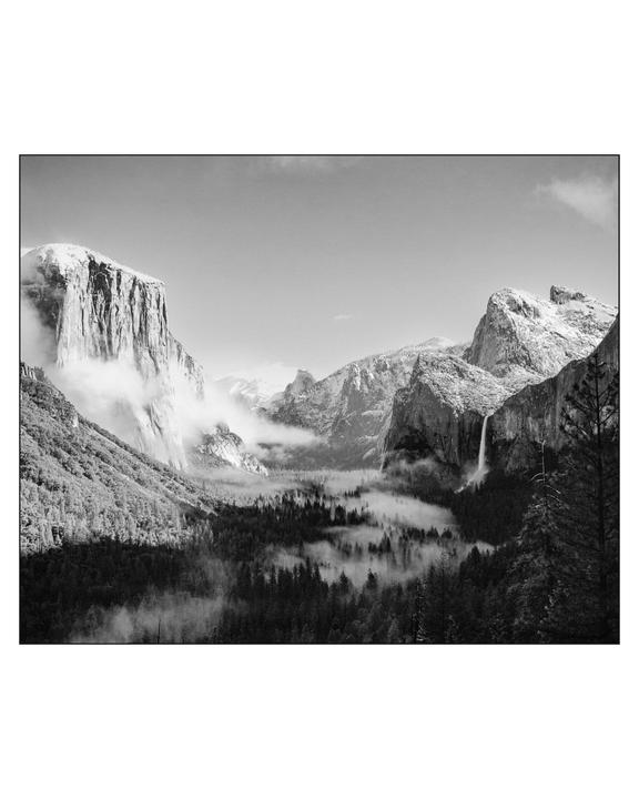 A black and white landscape shows a valley with a waterfall, surrounded by mountains and fog.