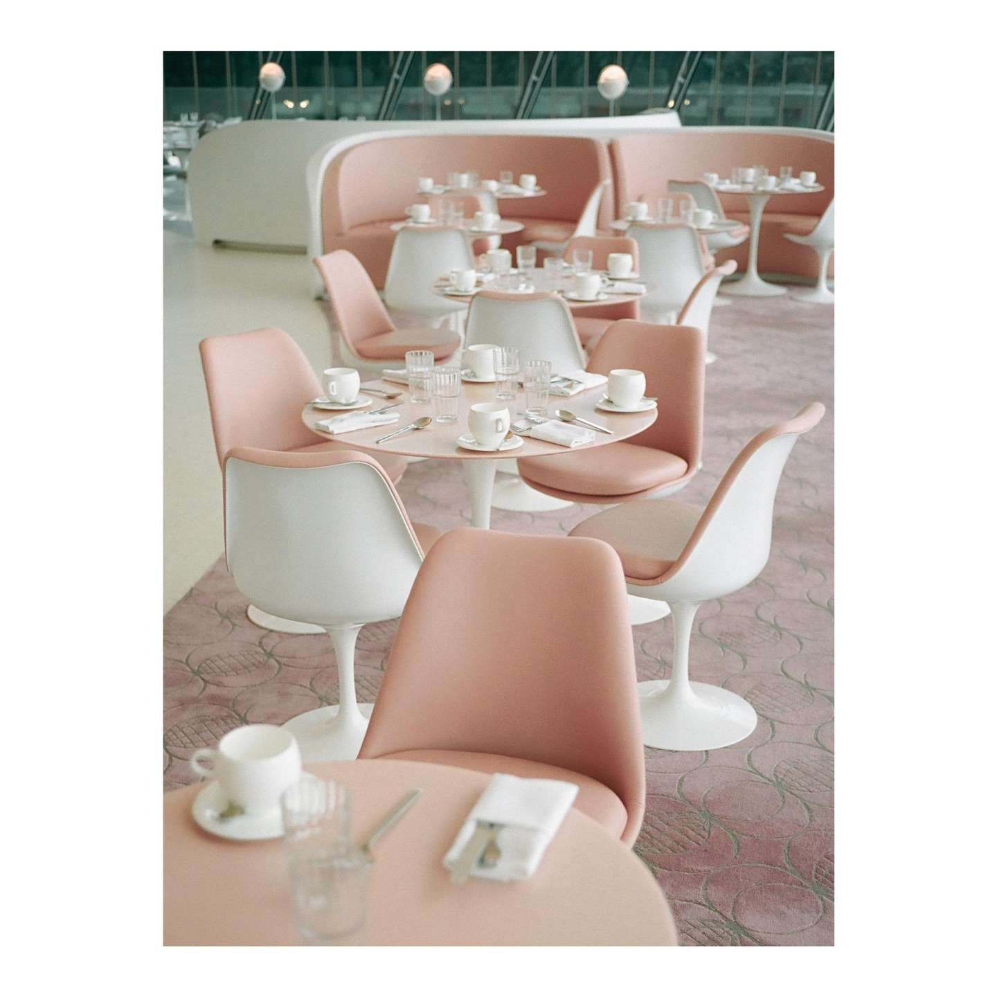 A cafe with pink tables and chairs is set with cups, glasses, and cutlery.