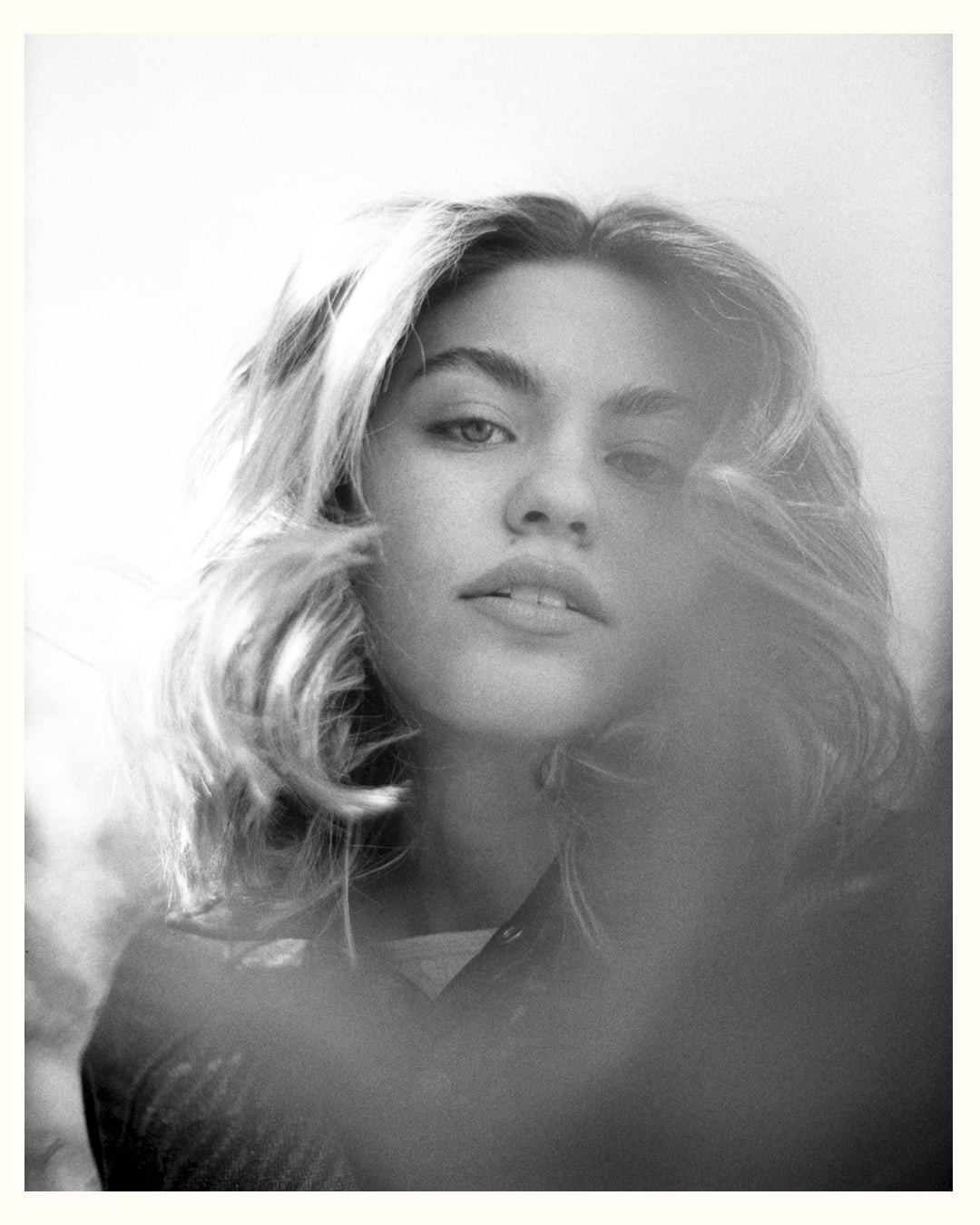 A woman with light hair looks directly at the viewer.