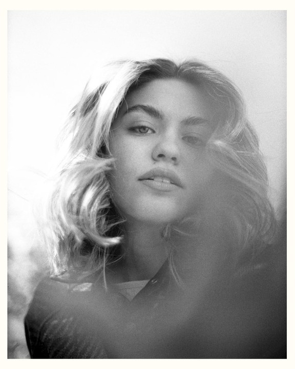 A woman with light hair looks directly at the viewer.