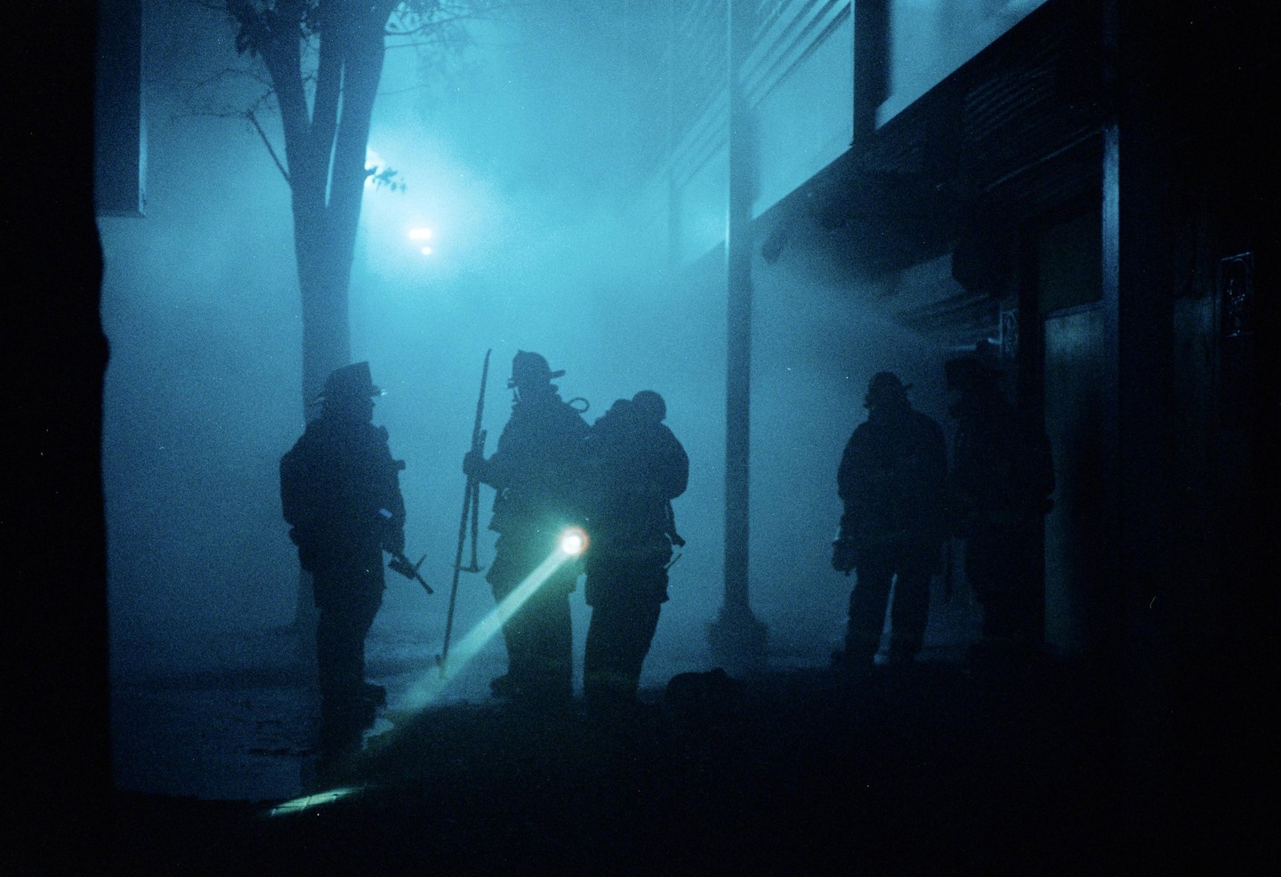 Several firefighters are silhouetted against a blue, hazy background at night.