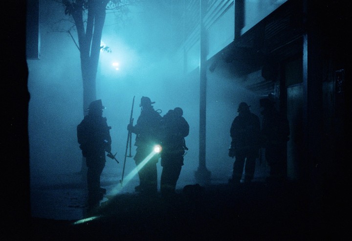 Several firefighters are silhouetted against a blue, hazy background at night.