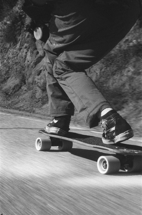 A person rides a skateboard down a road next to a rocky hillside.