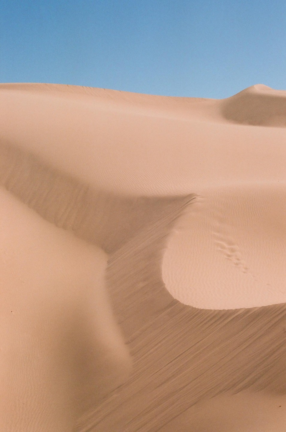 A large sand dune with ripples and shadows is visible under a clear blue sky.