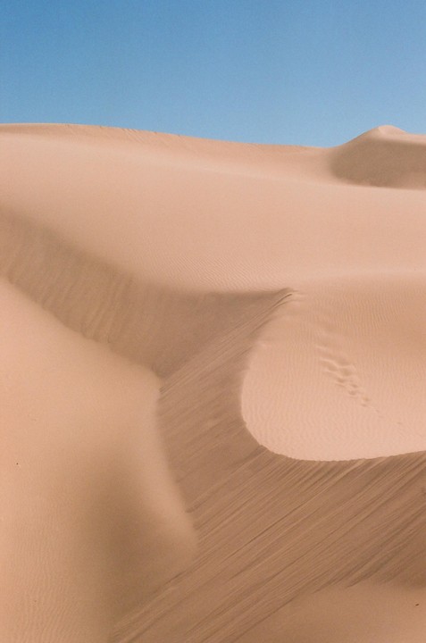 A large sand dune with ripples and shadows is visible under a clear blue sky.