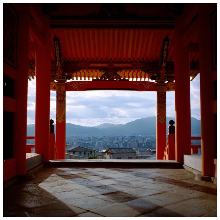 A city with mountains in the background is viewed from a red temple.