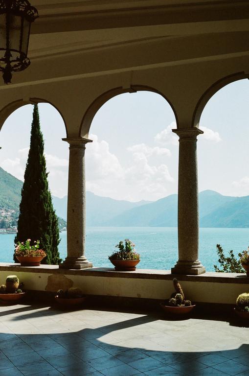 A balcony with arched columns overlooks a lake surrounded by mountains.