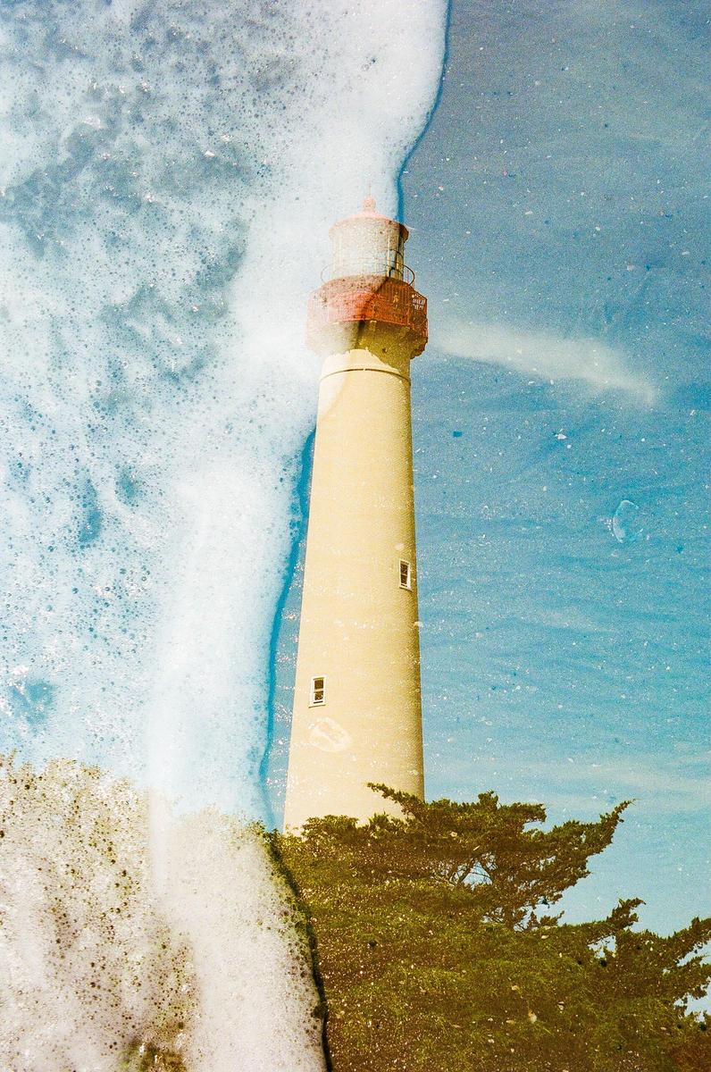 A double exposure shows a lighthouse superimposed over a foamy ocean wave.