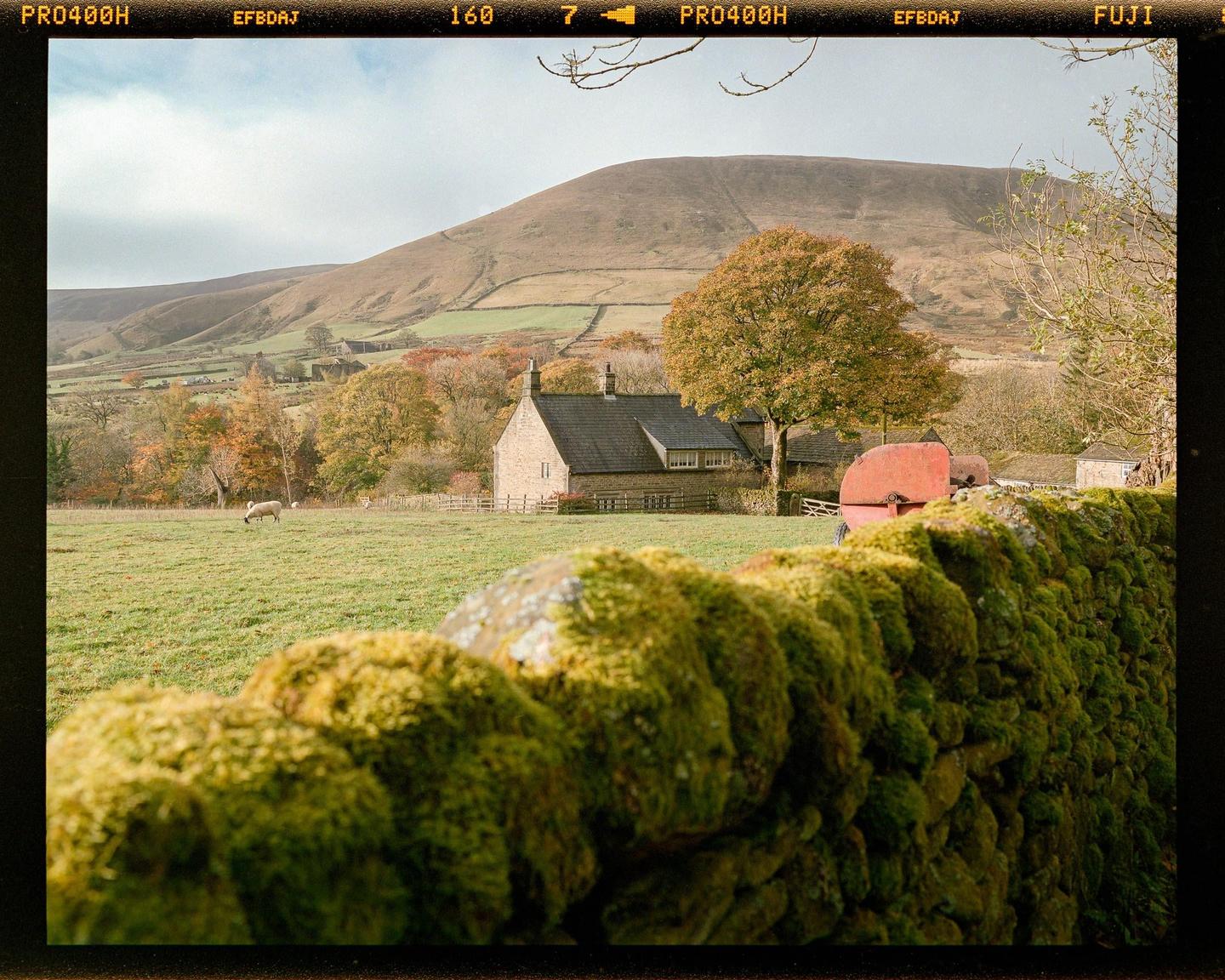 A moss-covered stone wall is in the foreground of a house and rolling hills.