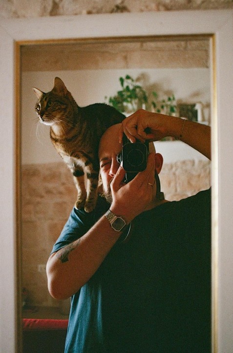 A man with a cat on his shoulder takes a mirror self-portrait.