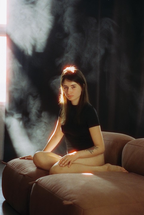 A woman sits on a sofa with light shining on her hair and body.