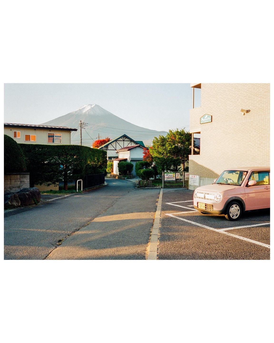 A pink car is parked on a street with Mount Fuji visible in the background.