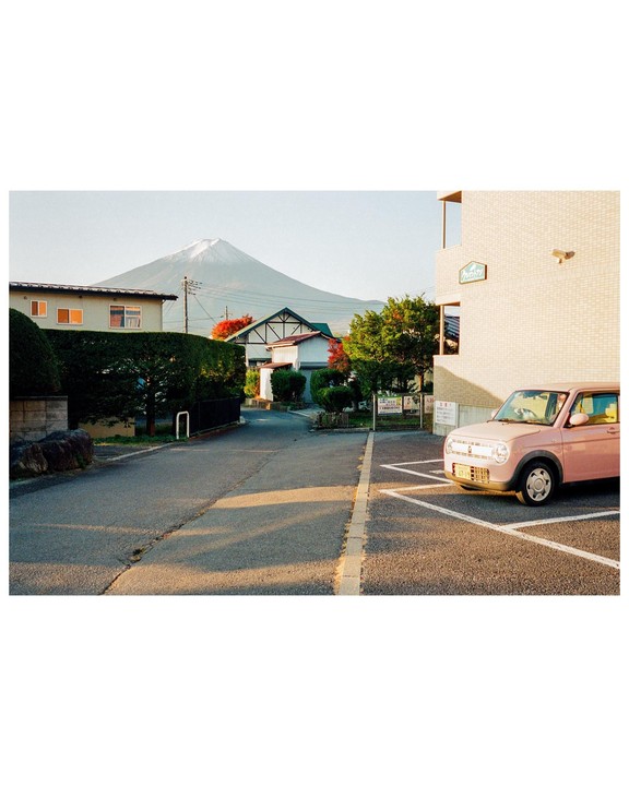 A pink car is parked on a street with Mount Fuji visible in the background.