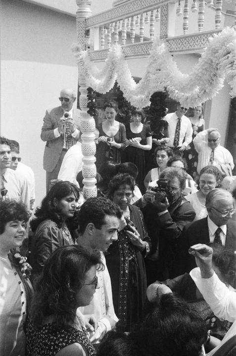 A crowd of people are gathered around a decorated structure, with some looking at the camera and others engaged in conversation.
