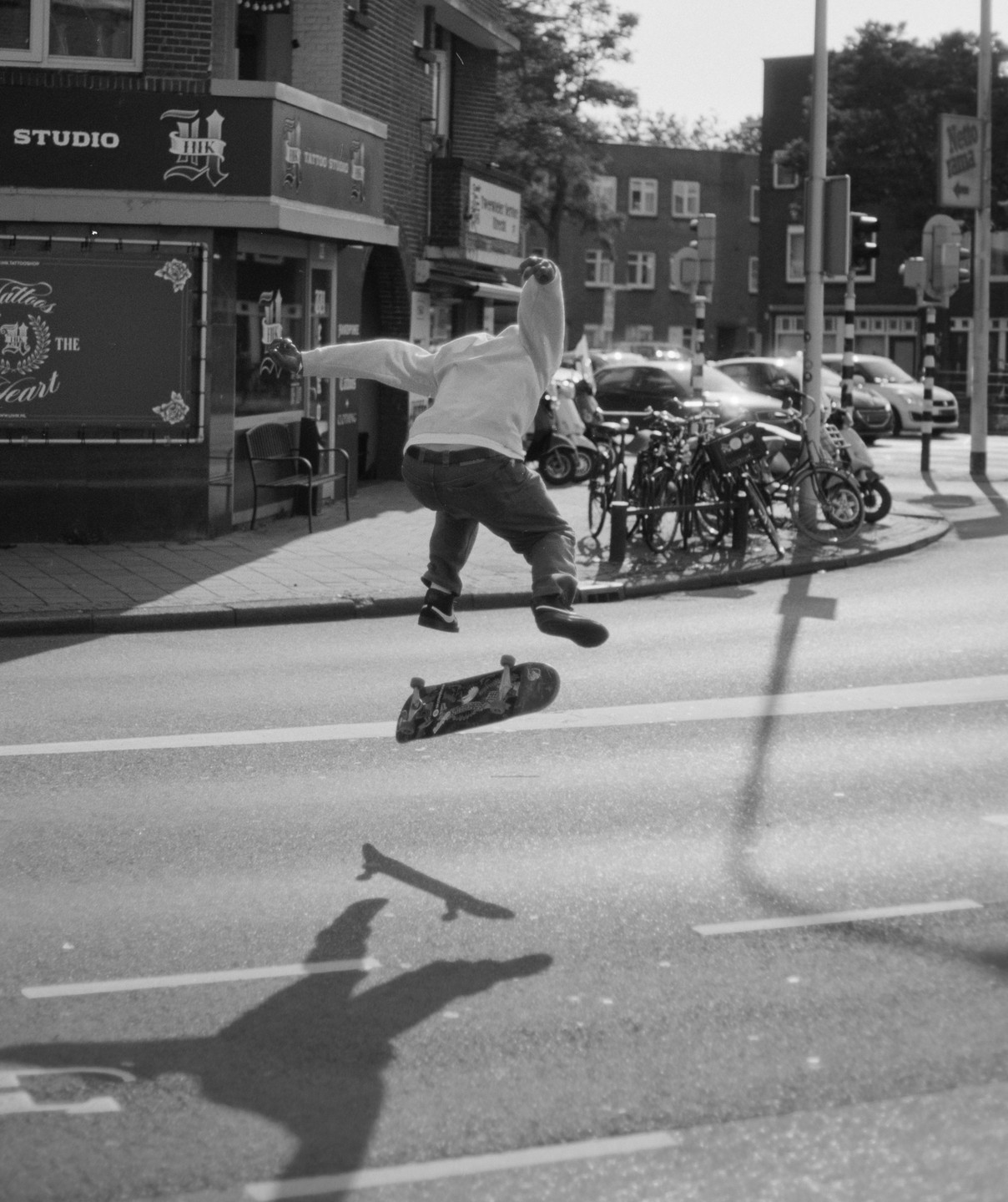 A boy jumps on a skateboard in the middle of a street next to a tattoo studio.