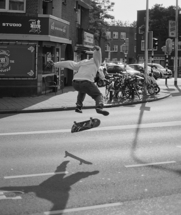 A boy jumps on a skateboard in the middle of a street next to a tattoo studio.