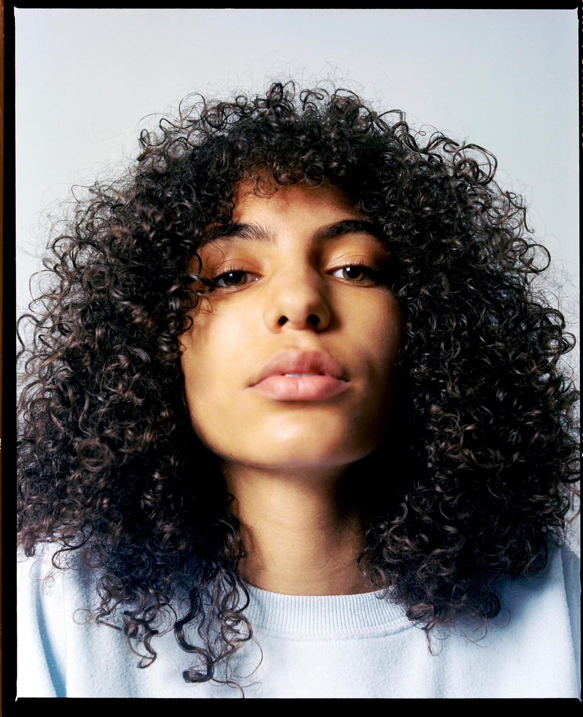 A woman with curly hair looks directly at the viewer.