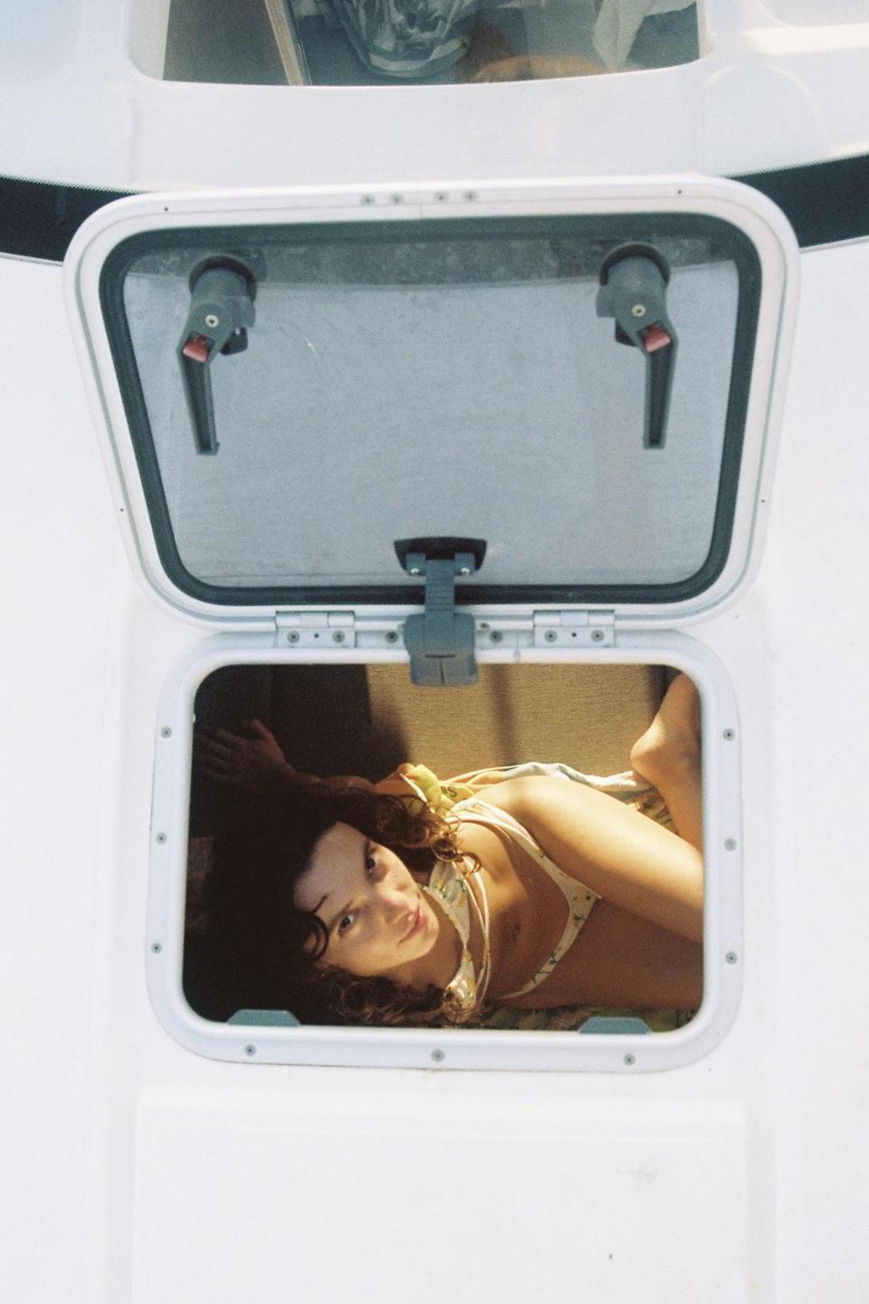 A woman in a bikini lies inside a boat cabin, looking up through an open hatch.