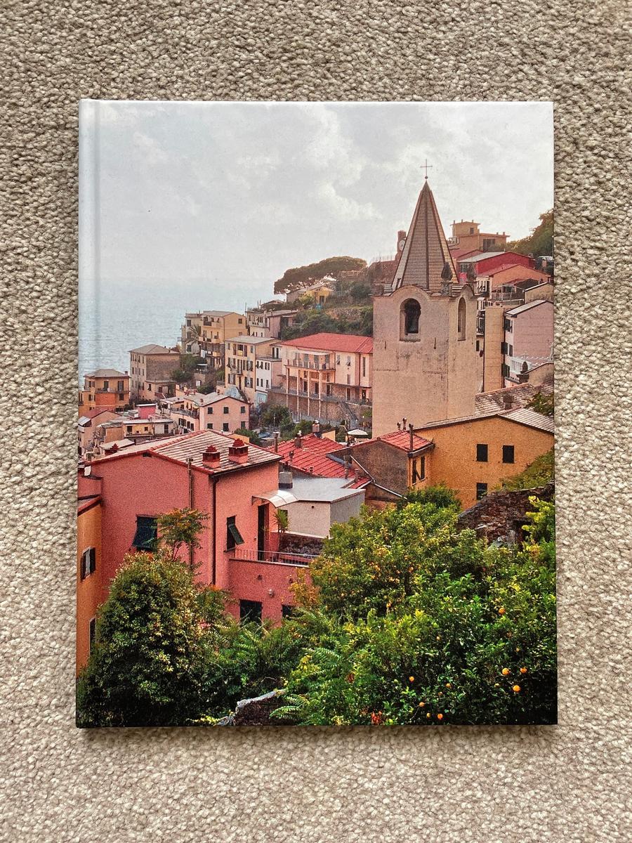 A book cover shows a hillside village with colorful buildings and a church steeple overlooking the sea.