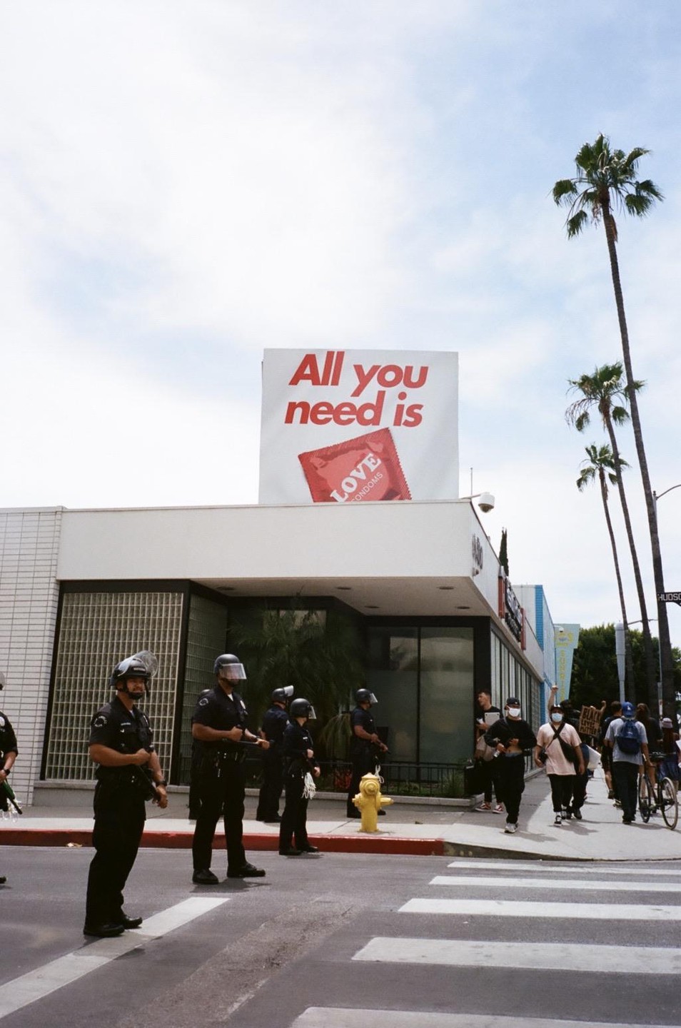 Police officers stand on a street corner with a billboard advertising condoms above them.