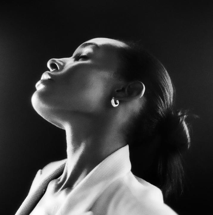 A woman with her head tilted back and eyes closed is illuminated by light from above.