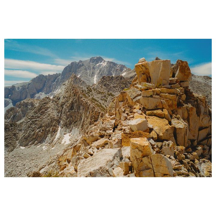 A mountain range with rocky peaks and patches of snow is visible under a blue sky.
