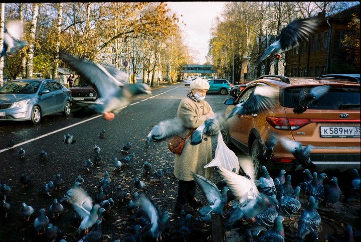 A woman in a coat and hat feeds pigeons on a street in Vologda.
