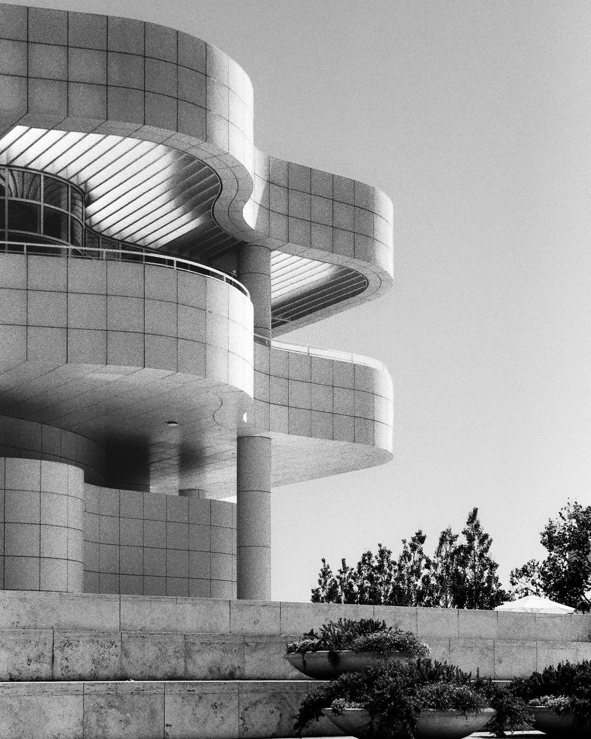 A modern building with curved walls and balconies stands above planters filled with greenery.