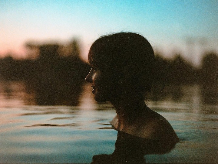 A woman is in water with her head and shoulders visible against a colorful sky.